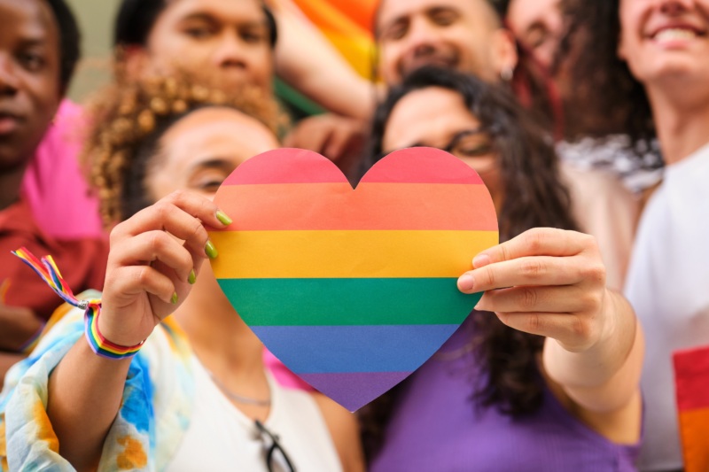 Two people holding a Rainbow Heart and People in the background, blurred